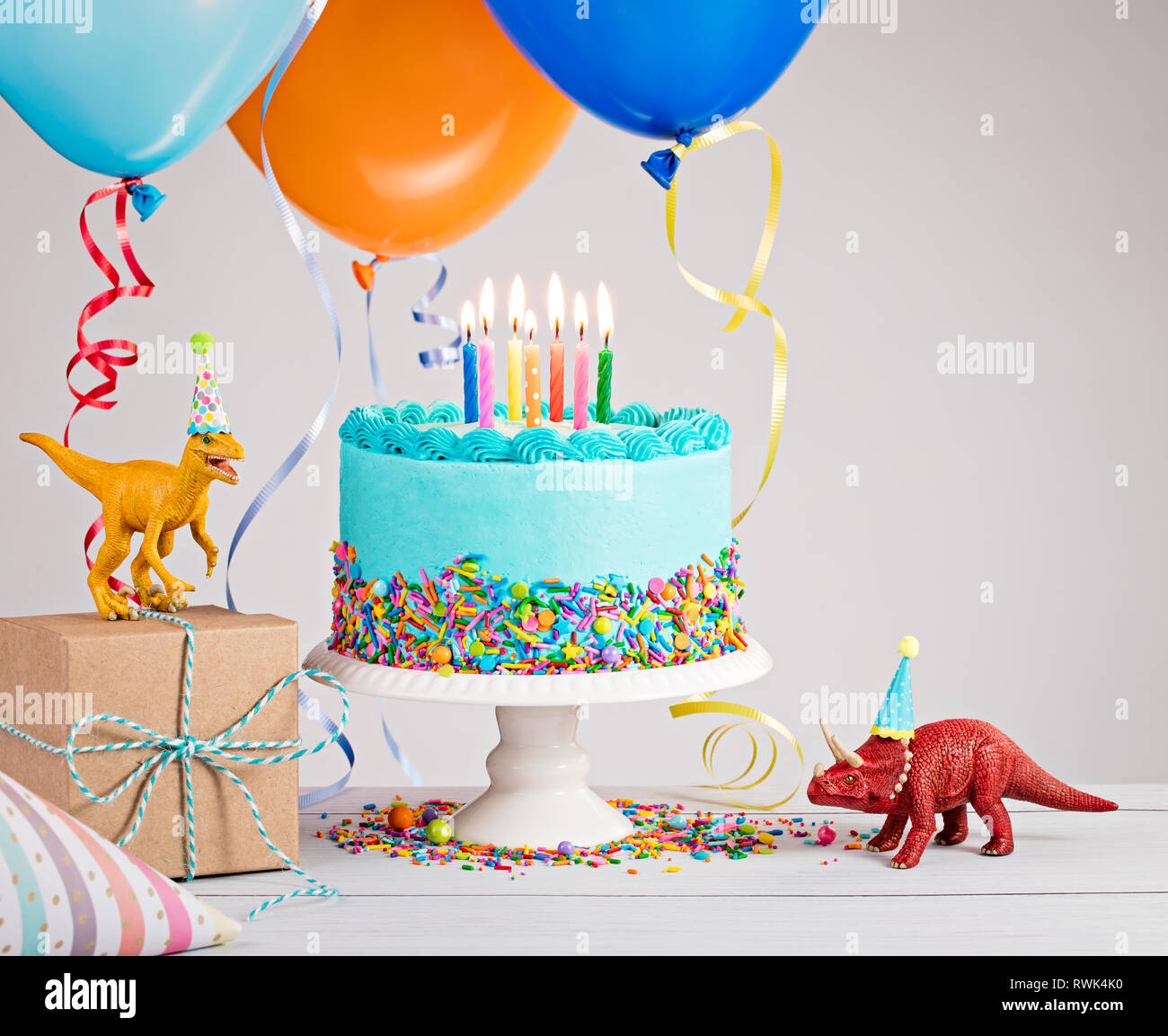 Childs festa di compleanno in scena con la torta blu confezione regalo giocattolo, dinosauri, cappelli e palloncini colorati su grigio chiaro. Foto Stock