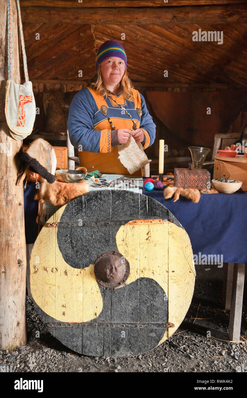 Reenactor in costume circondato da una varietà di realizzata a mano gli elementi che sarebbero stati tipicamente scambiati quando l'Anse aux Meadows fu colonizzata dai Vichinghi intorno all'anno 1000. Norstead Viking Village e il porto di commercio, l'Anse aux Meadows, Terranova, Canada Foto Stock