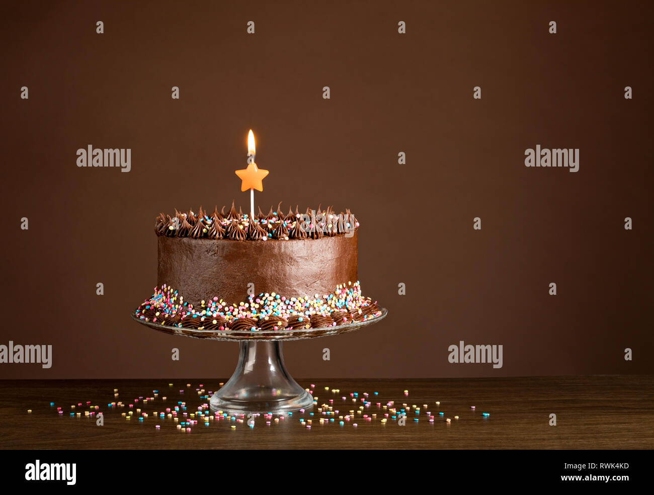 Cioccolato torta di compleanno con colorati spruzza e candele su sfondo di legno. Foto Stock
