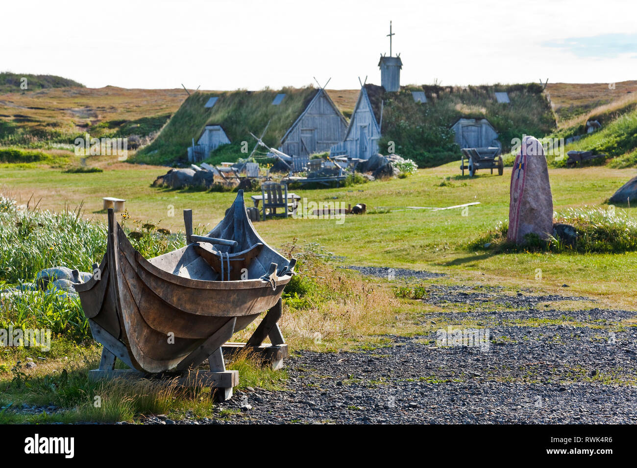 Un Norse faering (cioè un quattro-imbarcazione a remi) dietro il quale è un ricopra con zolle erbose-chiesa coperta ed un negozio di fabbro ferraio Norstead a Viking Villange e porto di commercio, l'Anse au Prati, Terranova, Canada Foto Stock