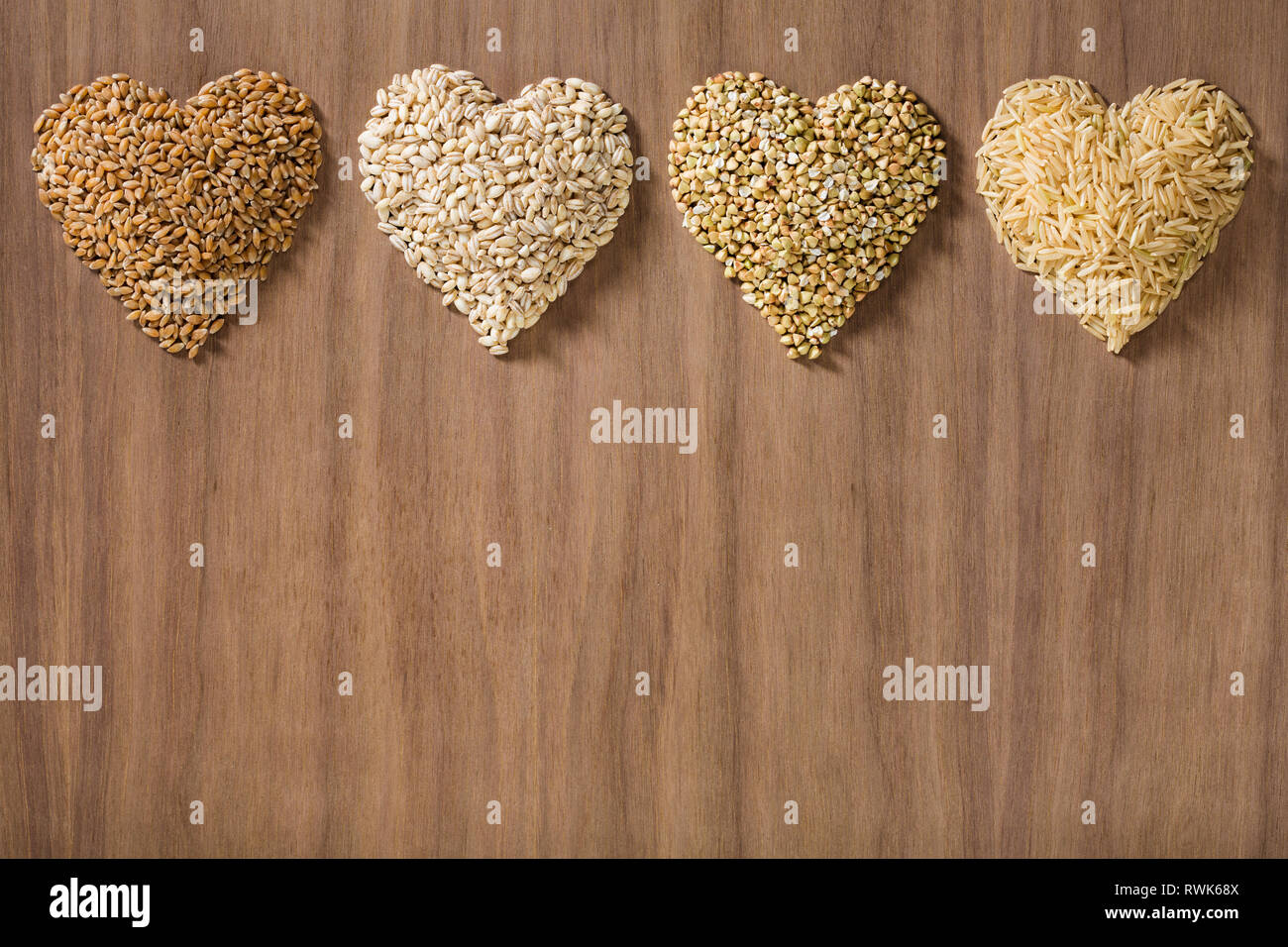 Una sana grani interi conformata come cuori su un sfondo di legno. Frumento, Orzo, grano saraceno e il riso marrone. Foto Stock