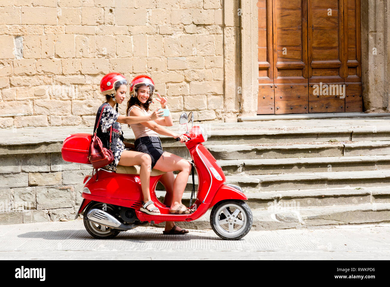 Amici prendendo selfie su scooter da ingresso della chiesa, Città della Pieve, Umbria, Italia Foto Stock
