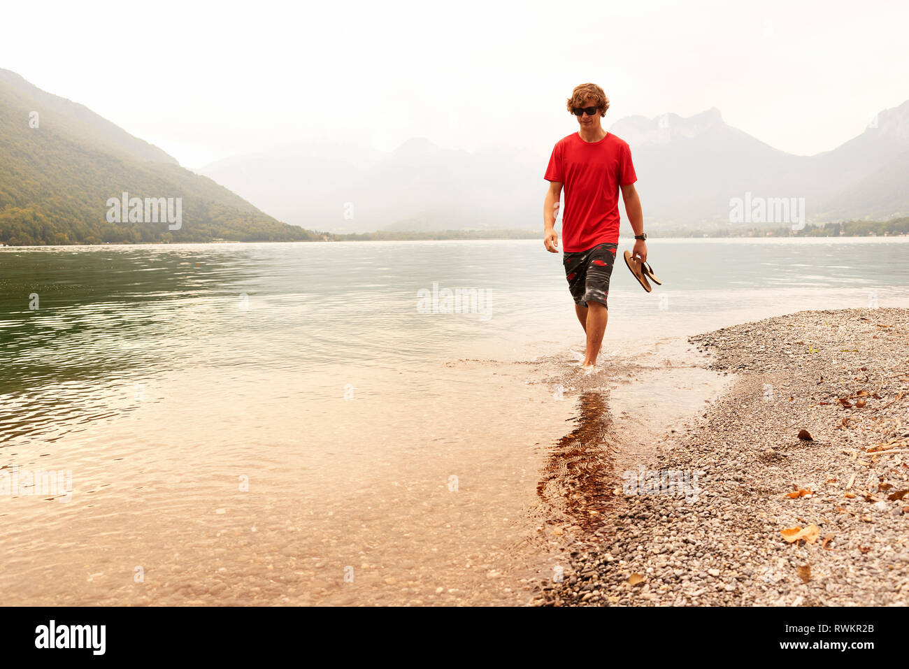 Giovane uomo paddling caviglia nel profondo del lago di Annecy, Annecy, Rhone-Alpes, Francia Foto Stock