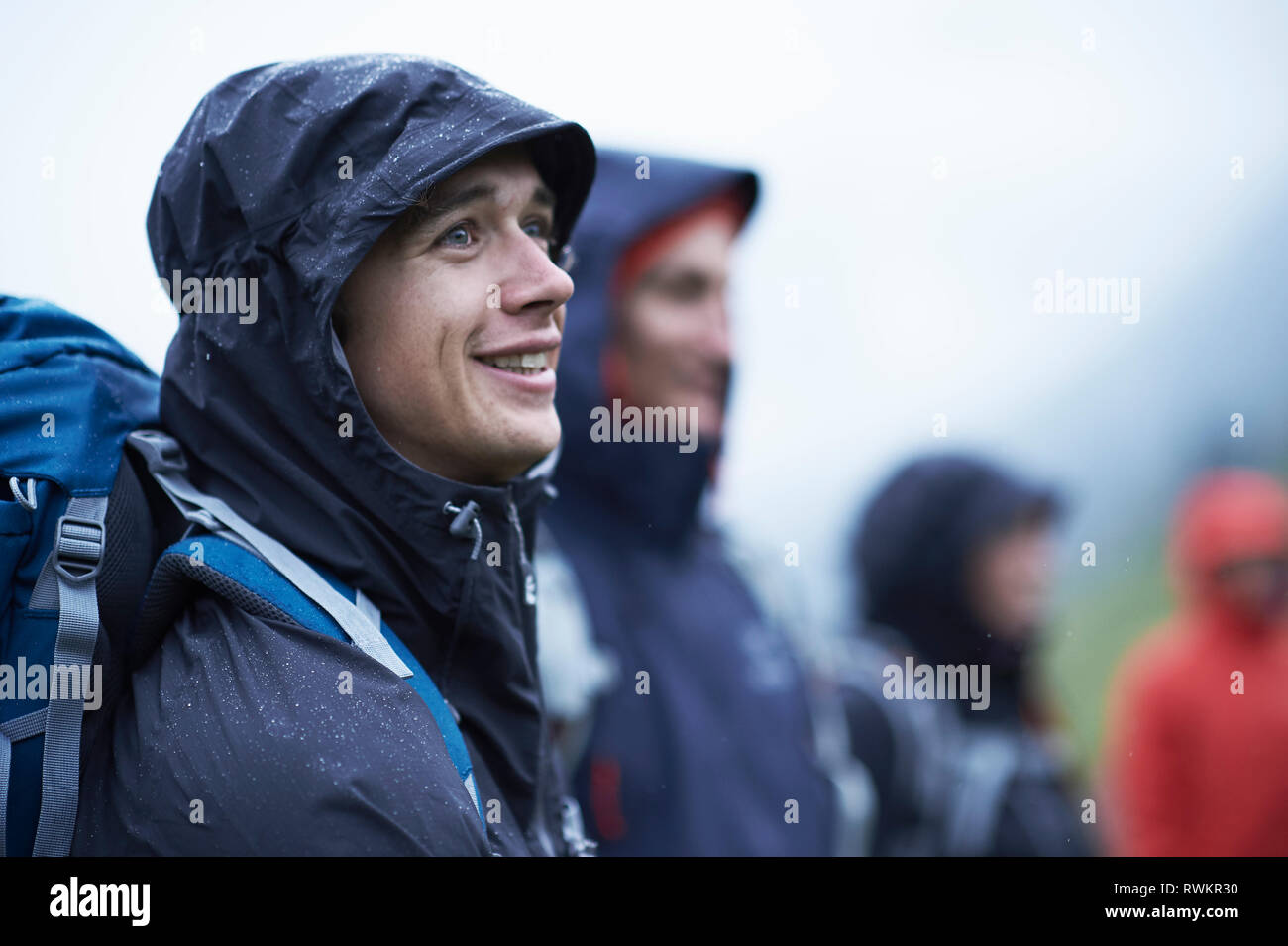 Giovane maschio escursionista con amici in hooded giacche a vento nella pioggia, Manigod, Rhone-Alpes, Francia Foto Stock