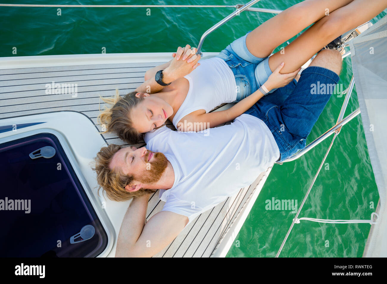 Coppia giovane giacente sulla barca a vela sul lago Chiemsee, vista aerea, Baviera, Germania Foto Stock