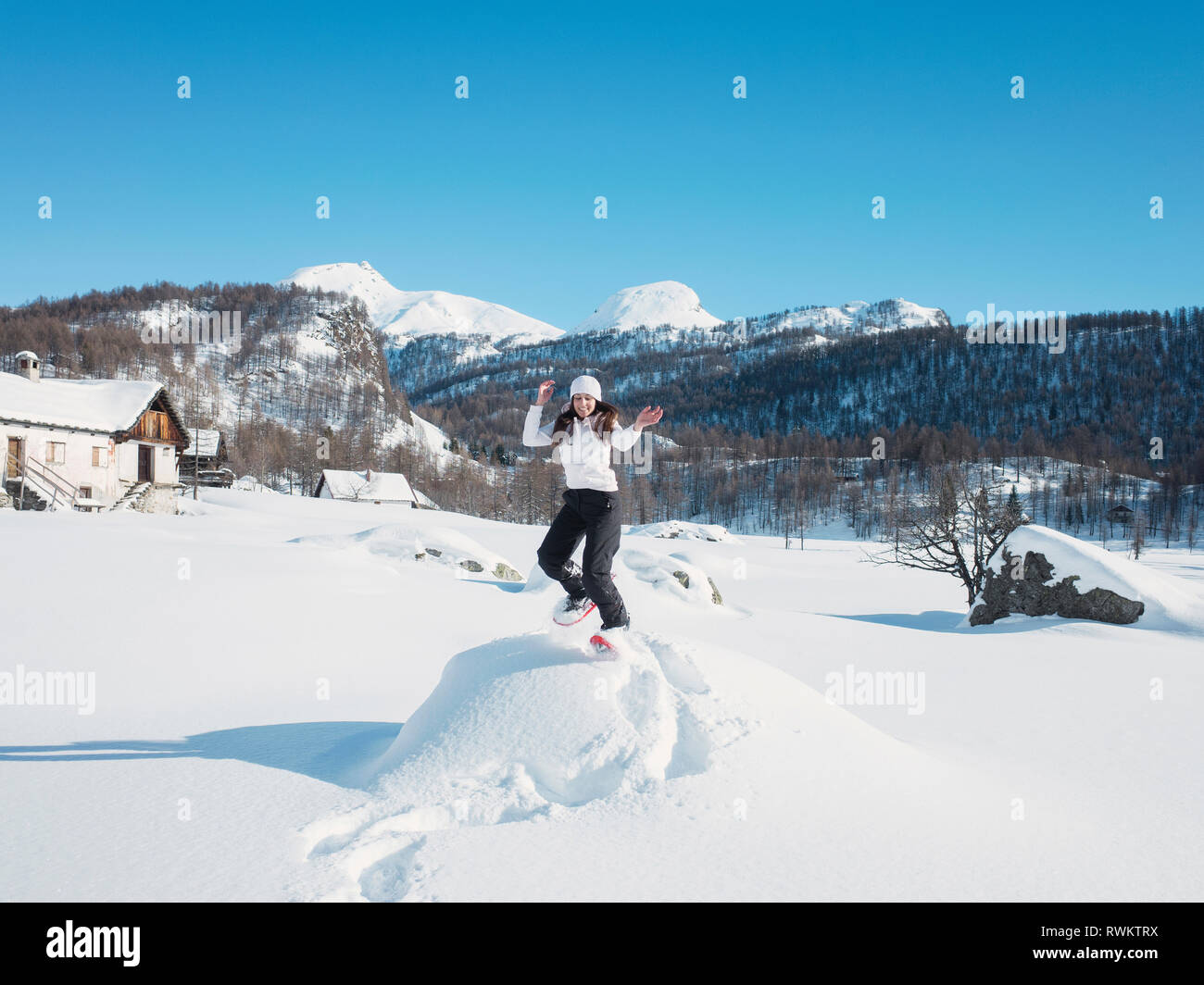 Giovane donna in knit hat jumping in paesaggi innevati, ritratto, Alpe Ciamporino, Piemonte, Italia Foto Stock