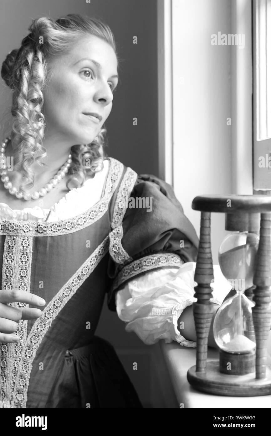 Ritratto di una giovane e bella donna in ornato abito storico- i suoi vestiti sono belle, sta in piedi da una porta nel profondo del pensiero e sembra triste. Foto Stock