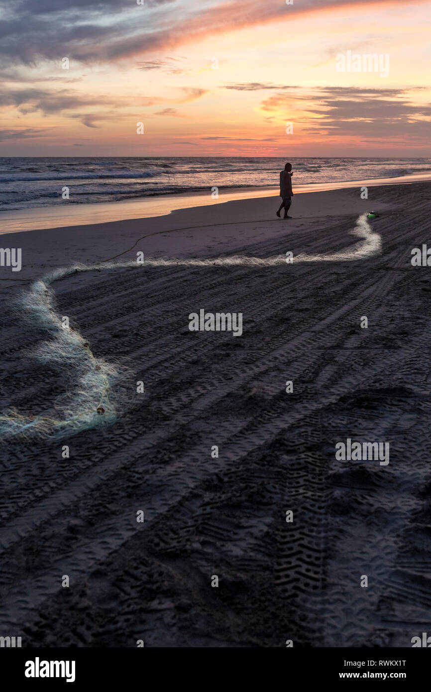 Un pescatore preparando la sua rete da pesca al tramonto su una spiaggia messicana Foto Stock