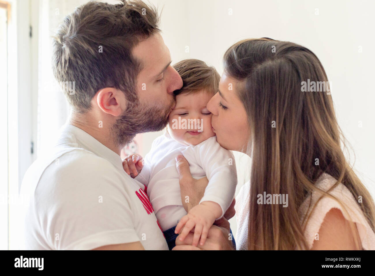 I genitori kissing Baby girl's guance a casa Foto Stock