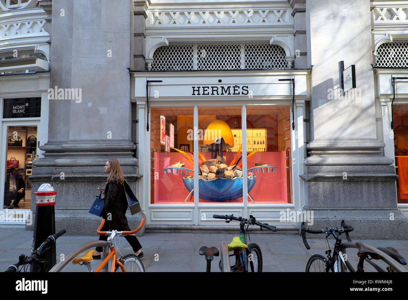 Una moda donna camminare al di fuori della Hermès Paris store boutique esterno vetrina in Royal Exchange, città di Londra Inghilterra KATHY DEWITT Foto Stock
