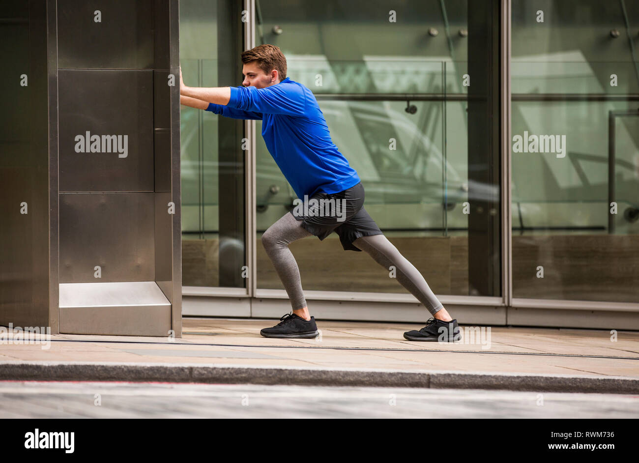 Giovani runner stretching sul marciapiede, London, Regno Unito Foto Stock