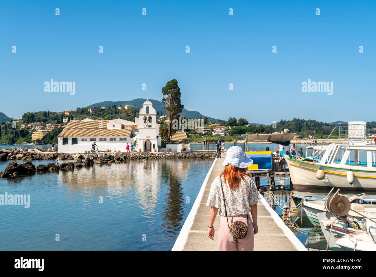 Tourist camminando sul ponte che conduce a Vlacherna Monastery, isola sullo sfondo, Corfù, Kerkira, Grecia Foto Stock