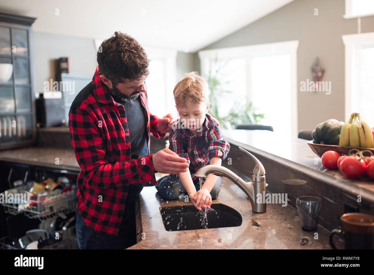 Padre guardando figlio di lavare le mani nel lavello da cucina Foto Stock
