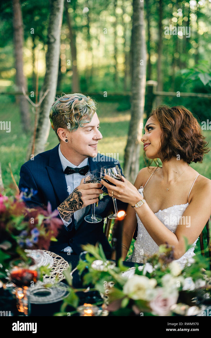 Sposa e lo sposo il sollevamento di un vetro al tavolo della foresta Foto Stock