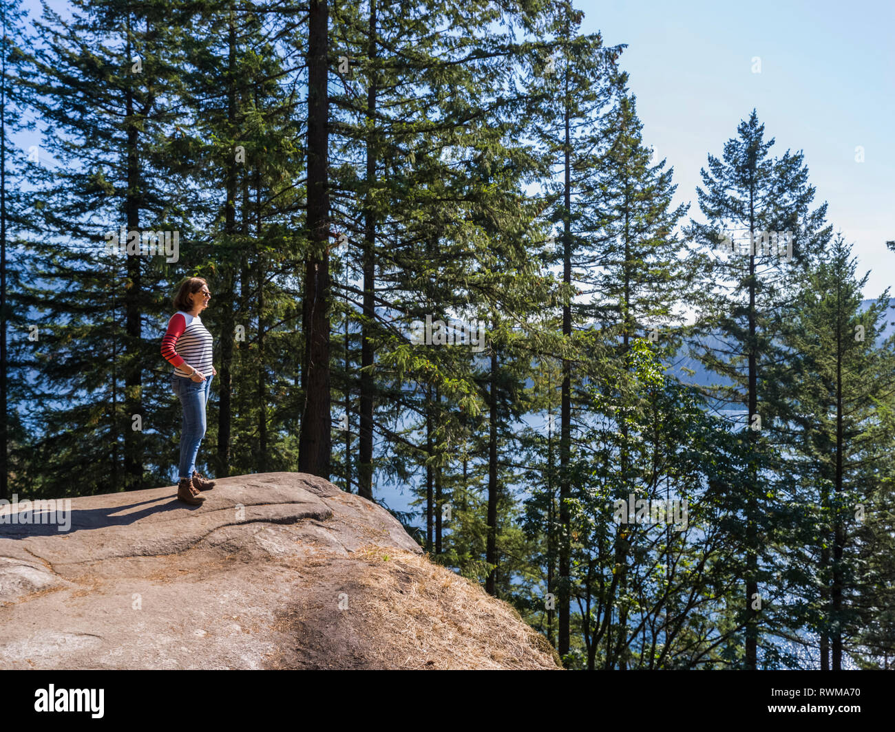 Una donna si erge a Cava sulla roccia Baden-Powell Trail guardando fuori per il litorale, Deep Cove, North Vancouver; Vancouver, British Columbia, Canada Foto Stock