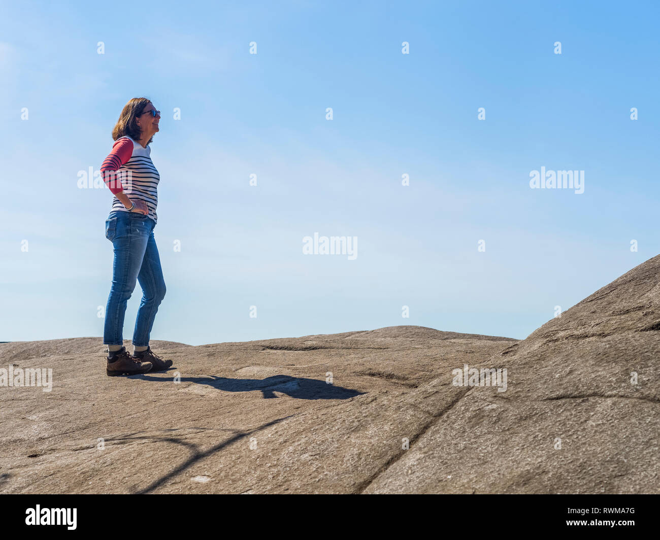 Una donna si erge a Cava sulla roccia Baden-Powell Trail contro un cielo blu, Deep Cove, North Vancouver; Vancouver, British Columbia, Canada Foto Stock