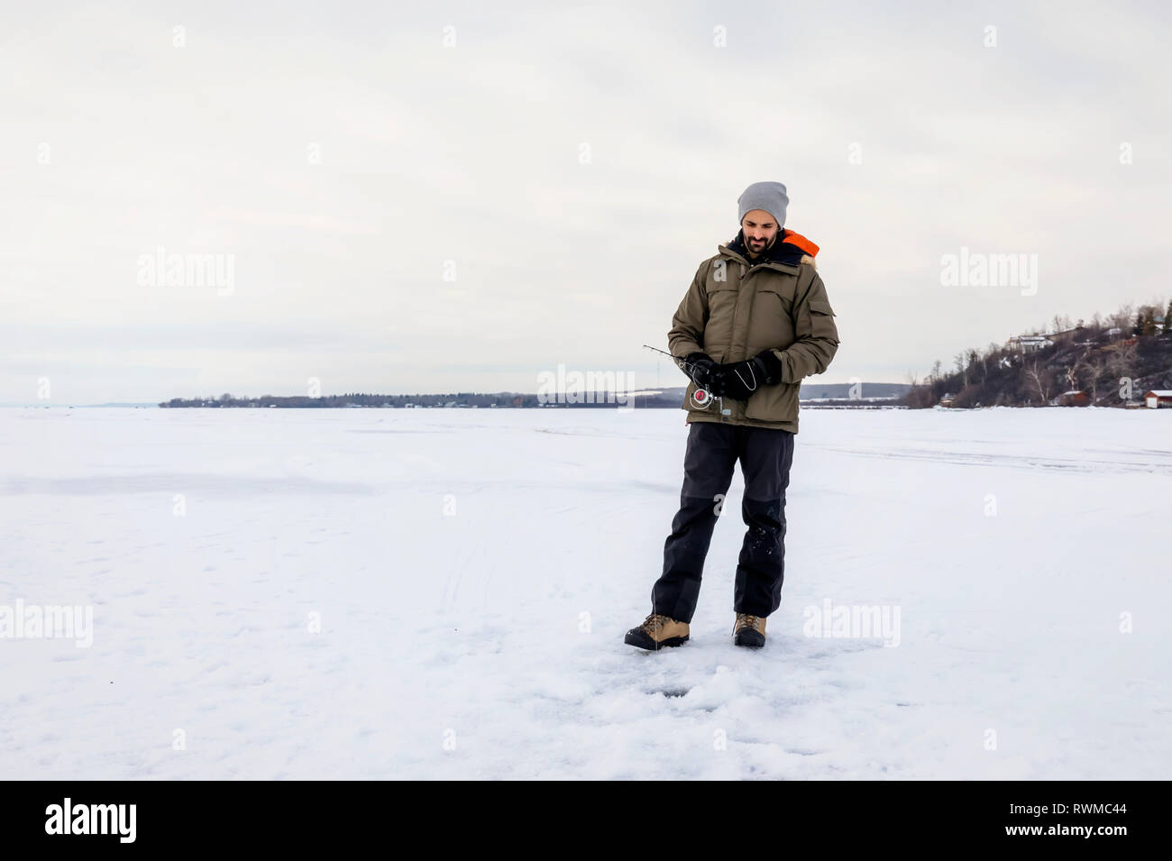 L'uomo aspettando pazientemente per un morso mentre la pesca sul ghiaccio al lago Wabamun; Wabamun, Alberta, Canada Foto Stock