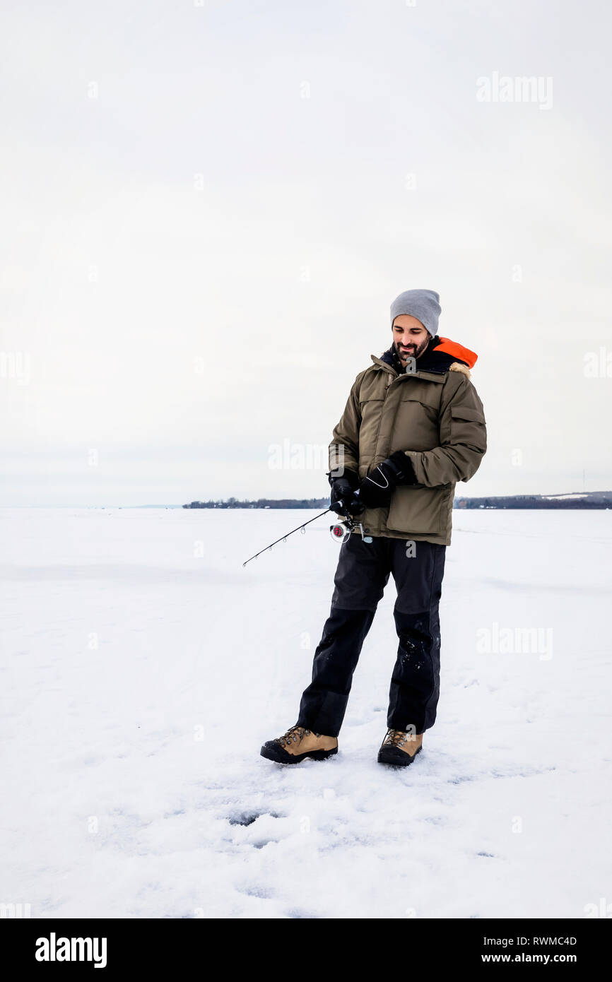 L'uomo aspettando pazientemente per un morso mentre la pesca sul ghiaccio al lago Wabamun; Wabamun, Alberta, Canada Foto Stock