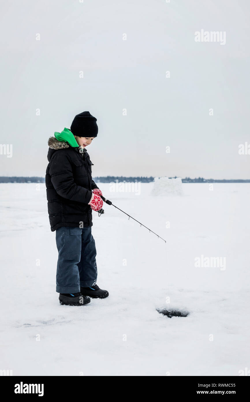 Ragazzo aspettando pazientemente per un morso mentre la pesca sul ghiaccio al lago Wabamun; Wabamun, Alberta, Canada Foto Stock