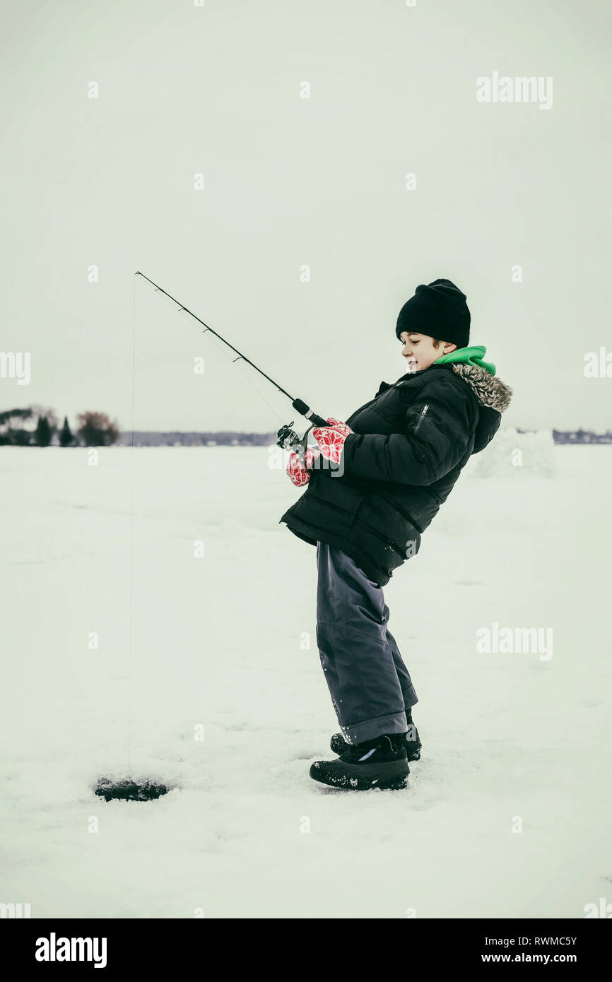 Un giovane ragazzo la pesca sul ghiaccio e ottiene un morso mentre la pesca sul ghiaccio al lago Wabamun; Wabamun, Alberta, Canada Foto Stock