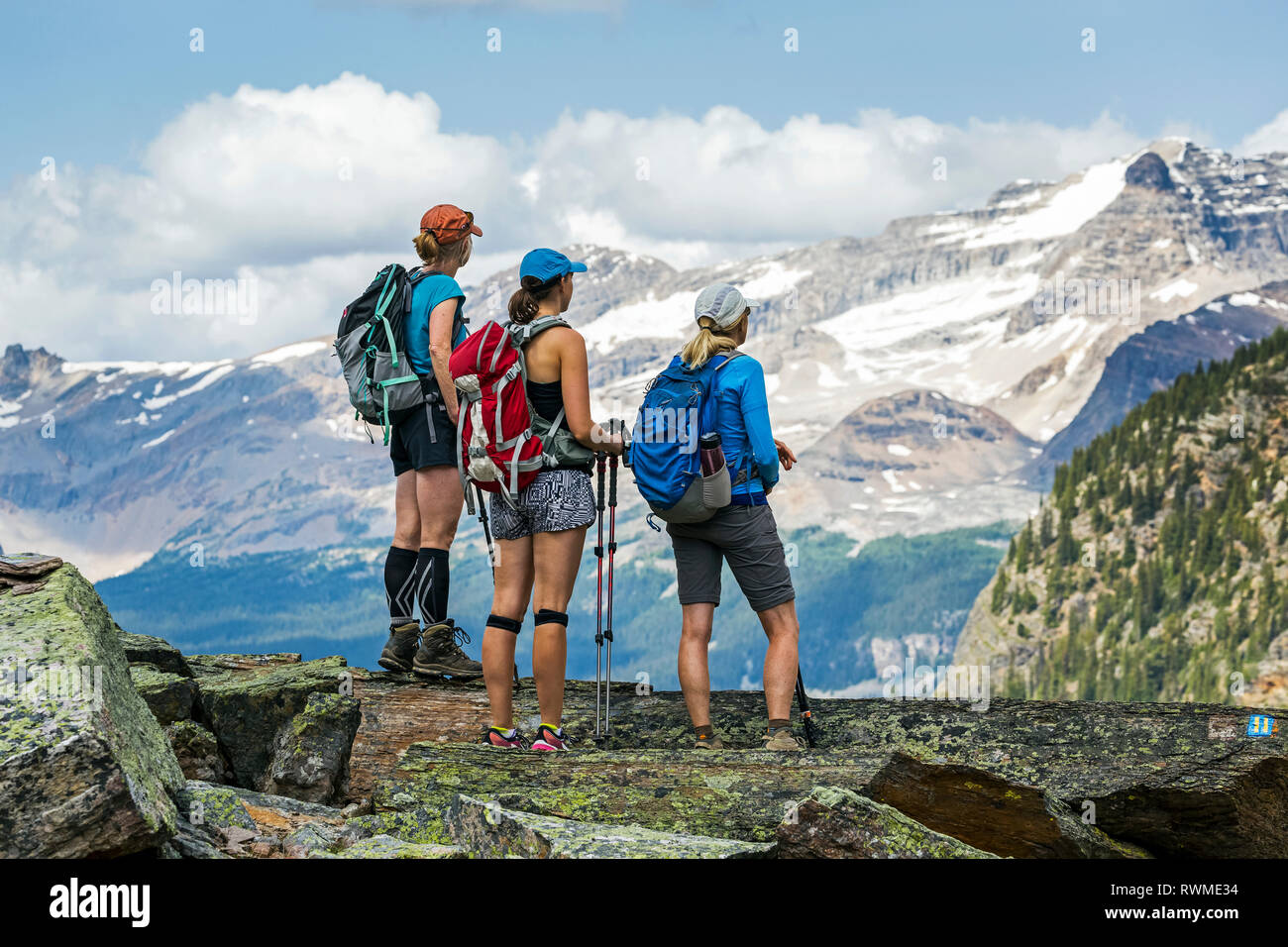 Tre escursionisti femmina su una roccia di montagna che si affaccia mountain vista in background; British Columbia, Canada Foto Stock