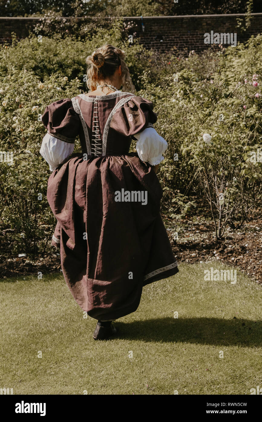 Ritratto di una giovane e bella donna in ornato abito storico- i suoi vestiti sono belle, lei è nel giardino di rose a Hampton Court Palace. Foto Stock