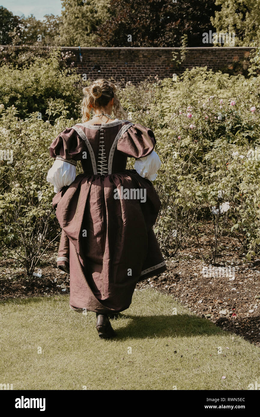 Ritratto di una giovane e bella donna in ornato abito storico- i suoi vestiti sono belle, lei è nel giardino di rose a Hampton Court Palace. Foto Stock