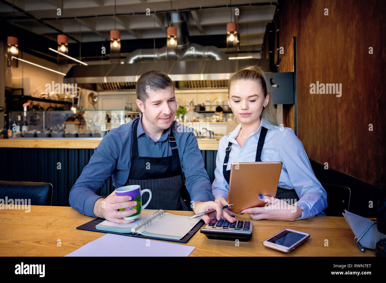 L uomo e la donna che indossa il grembiule facendo i conti dopo ore in un piccolo ristorante. I dipendenti controllo relazioni mensili Foto Stock