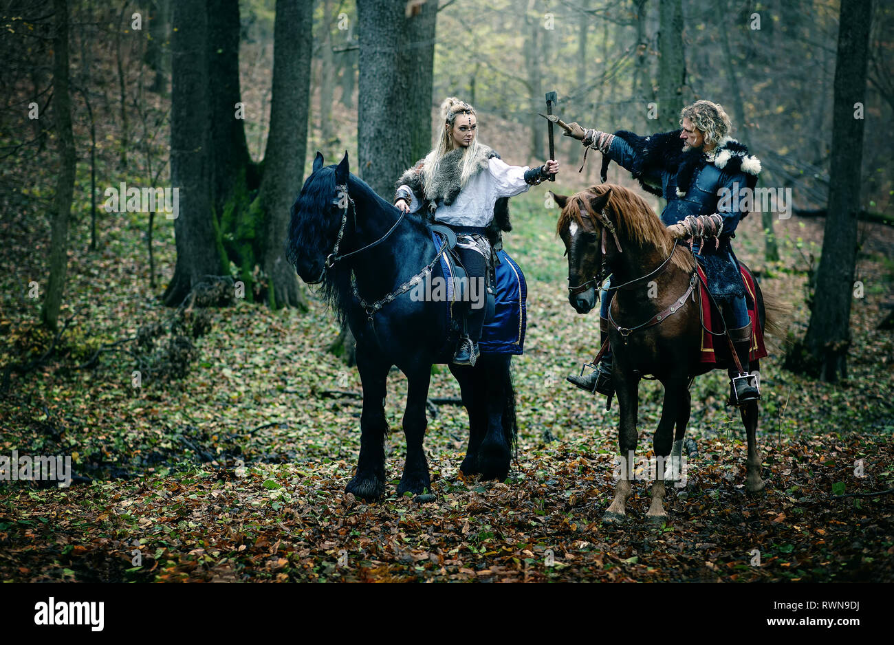 Guerrieri donna un uomo a cavallo nei boschi. Vichinghi scandinavi di equitazione con assi in mani. Abiti tradizionali con collare in pelliccia. Reconstructio Foto Stock