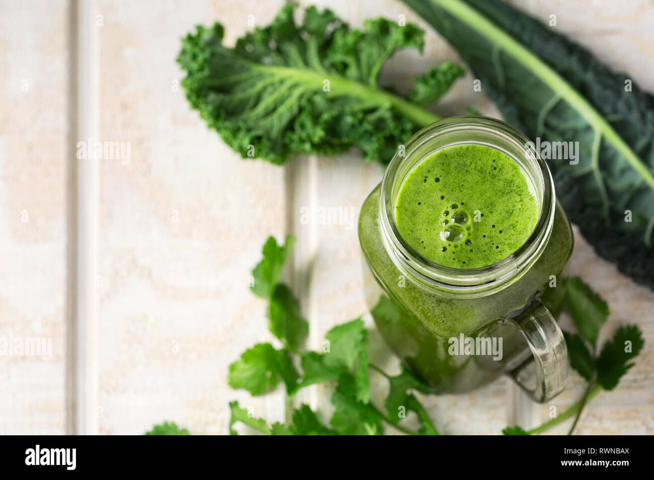 Succo verde realizzato da kale e coriandolo su un bianco superficie in legno con spazio di copia Foto Stock