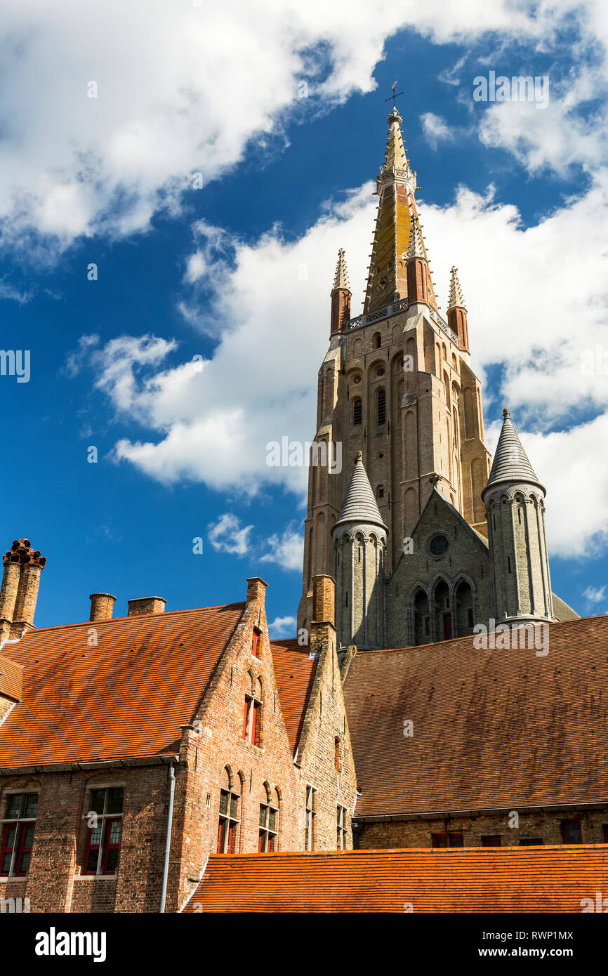 Alto campanile della chiesa di Nostra Signora nella città medievale di Bruges con il cielo blu e nuvole; Bruges, Belgio Foto Stock