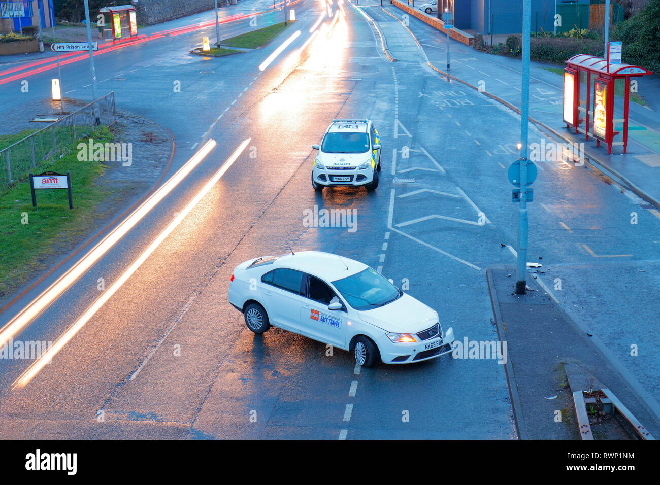 Un noleggio privato veicolo siede su una strada a doppia carreggiata a Leeds, custodito da un auto della polizia, dopo la collisione con una barriera di protezione. Foto Stock