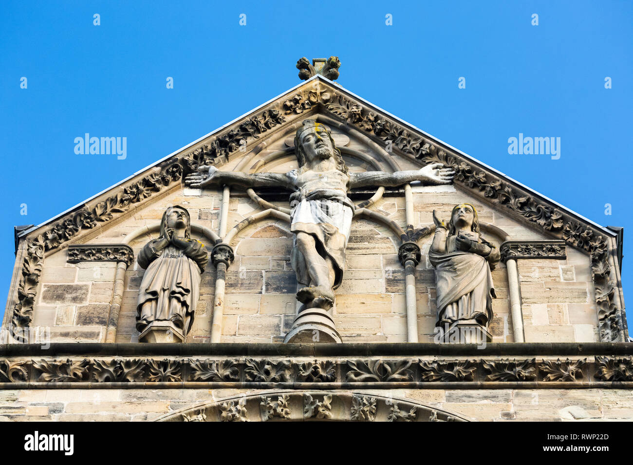 Close-up del crocifisso sulla parte superiore della chiesa di pietra ha raggiunto un picco facciata con cielo blu; Trier, Germania Foto Stock