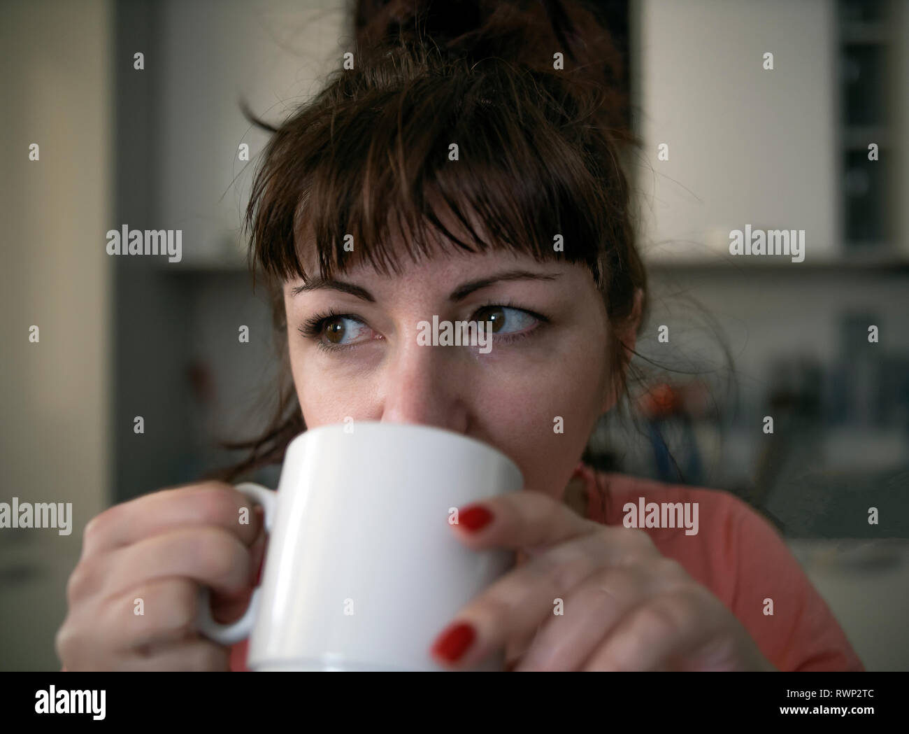 Giovane donna beve caffè al mattino in cucina, stanchi occhi con venature rosse, close-up Foto Stock