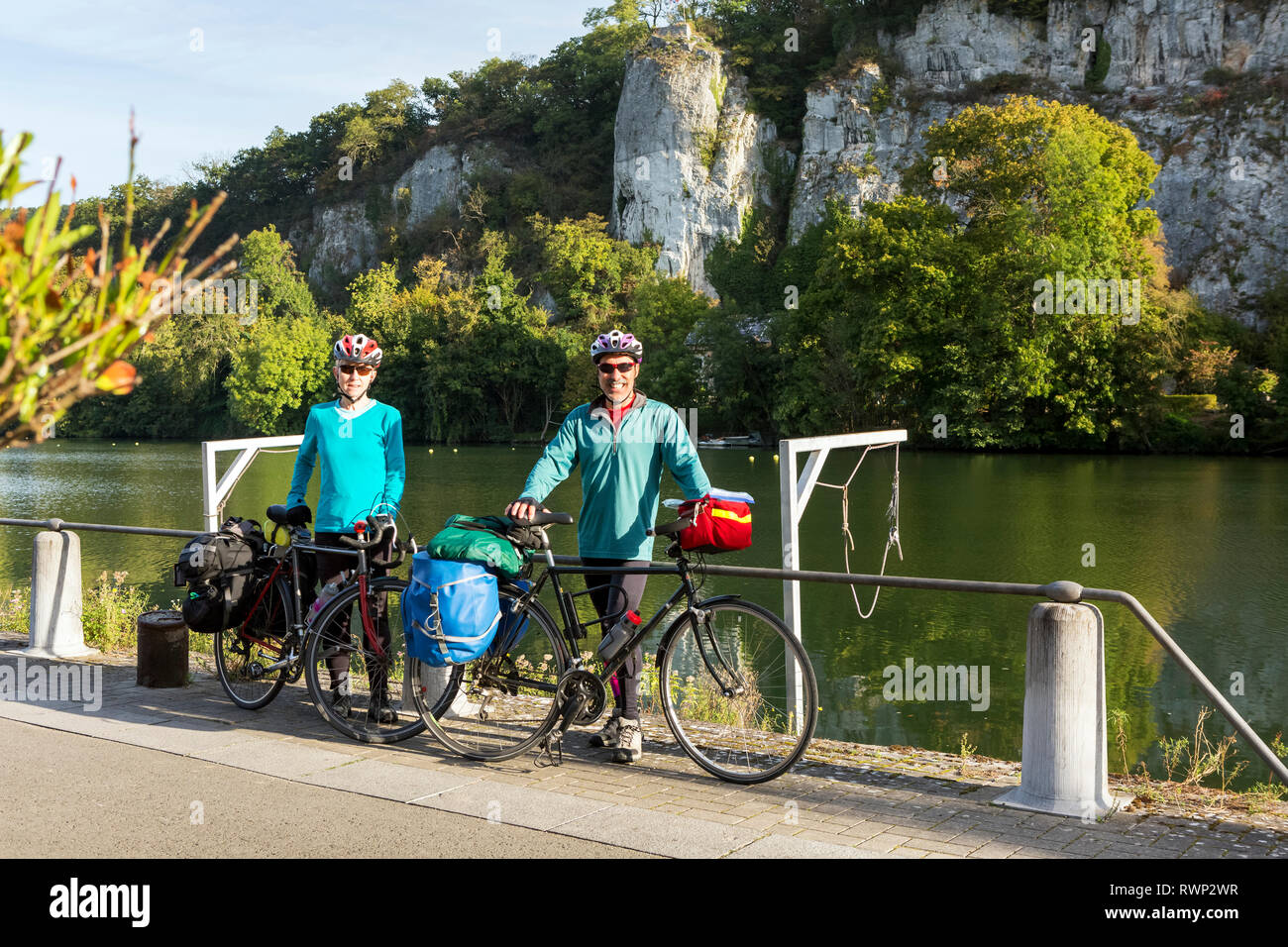 Maschi e femmine di ciclista permanente sulla pista ciclabile lungo una ringhiera di banca di fiume con scogliere in background e cielo blu, a sud di Namur, Belgio Foto Stock