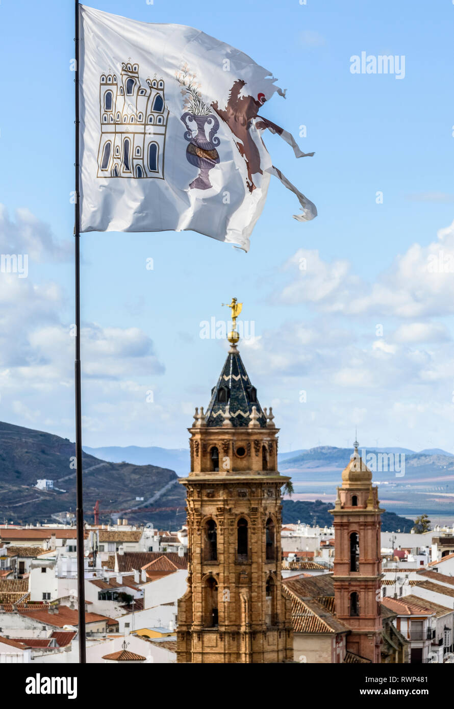 La città di Antequera con torri della chiesa e un RIP, weathered bandiera in primo piano; Antequera, Malaga, Spagna Foto Stock