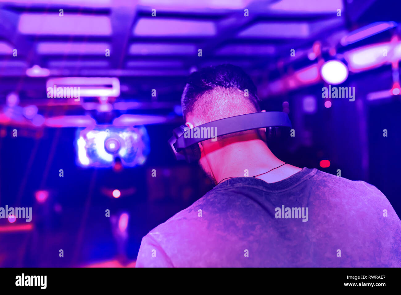 Sfocata defocalizzata del giovane maschio disc jockey di miscelazione e miscelazione di brani musicali sul suo ponte nelle tenebre di una parte o di un night club.Copia spazio per il testo. Foto Stock