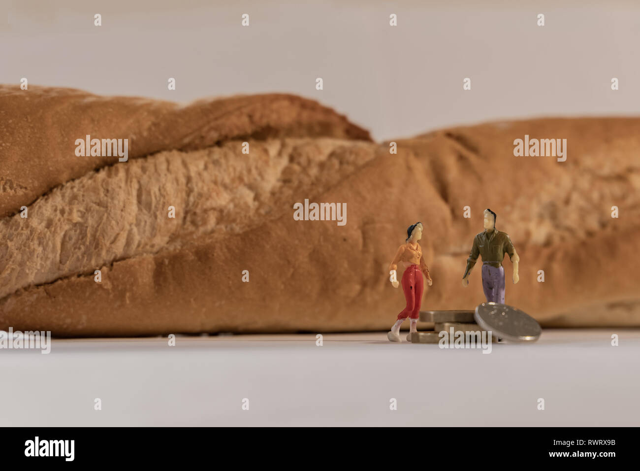 Miniatura donna e uomo figura in piedi accanto a grandi baguette di pane e il conteggio delle monete in euro. Profondità di campo per lo sfondo. Bilancio familiare sano, vite Foto Stock