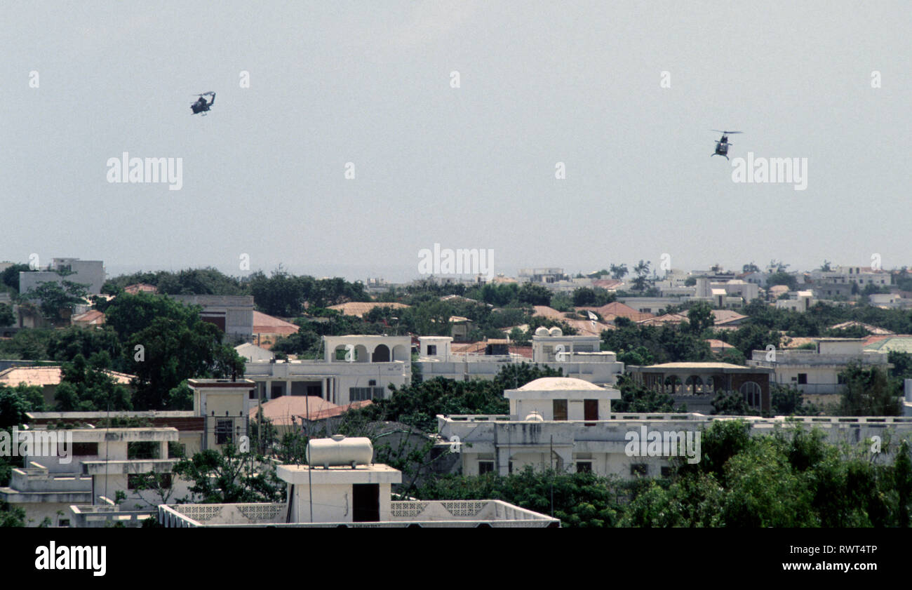 Xx Ottobre 1993 U.S. Esercito Bell AH-1 elicottero Cobra e un OH-58 Kiowa osservazione Scout elicottero di pattuglia di basso sopra i tetti di Mogadiscio, Somalia. Foto Stock