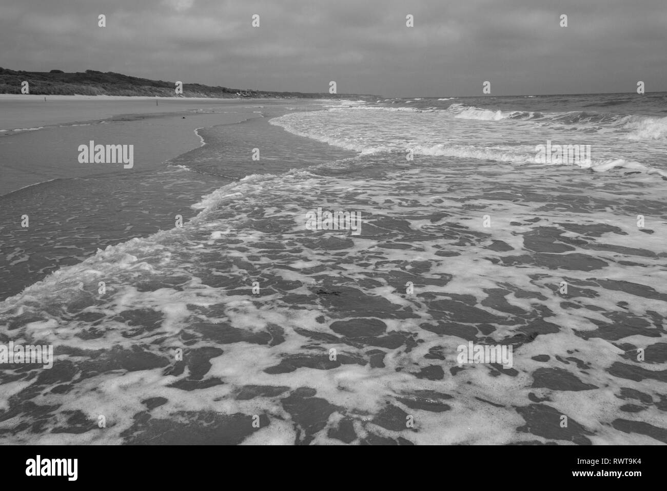 Onde che si infrangono sulla spiaggia sabbiosa (in B&W) che è la spiaggia di Omaha in Normandia vicino a Colleville-sur-Mer, Francia. Foto Stock