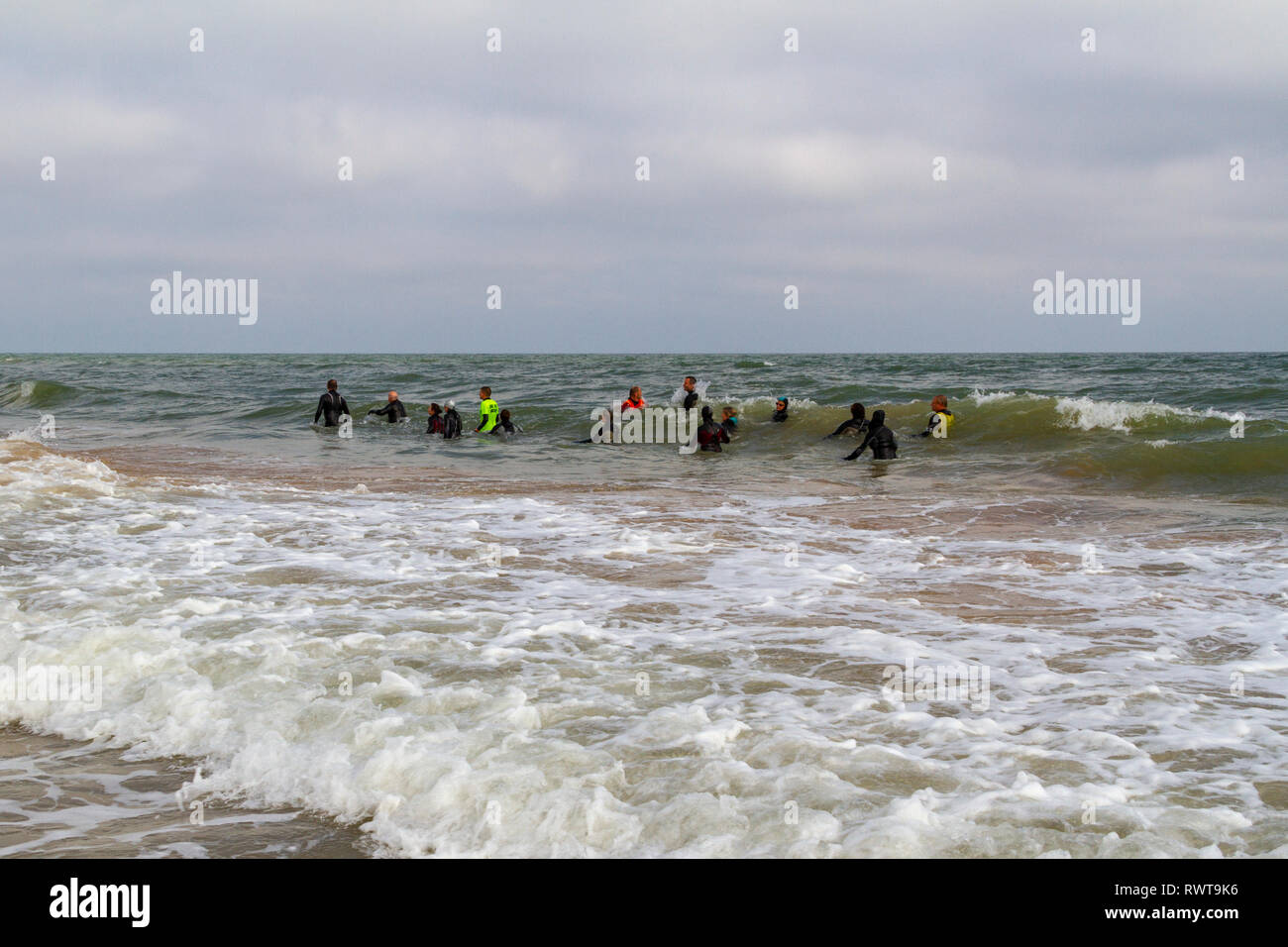 Un gruppo di grandi dimensioni a piedi attraverso il surf lungo la spiaggia in Normandia vicino a Colleville-sur-Mer, Francia. Foto Stock
