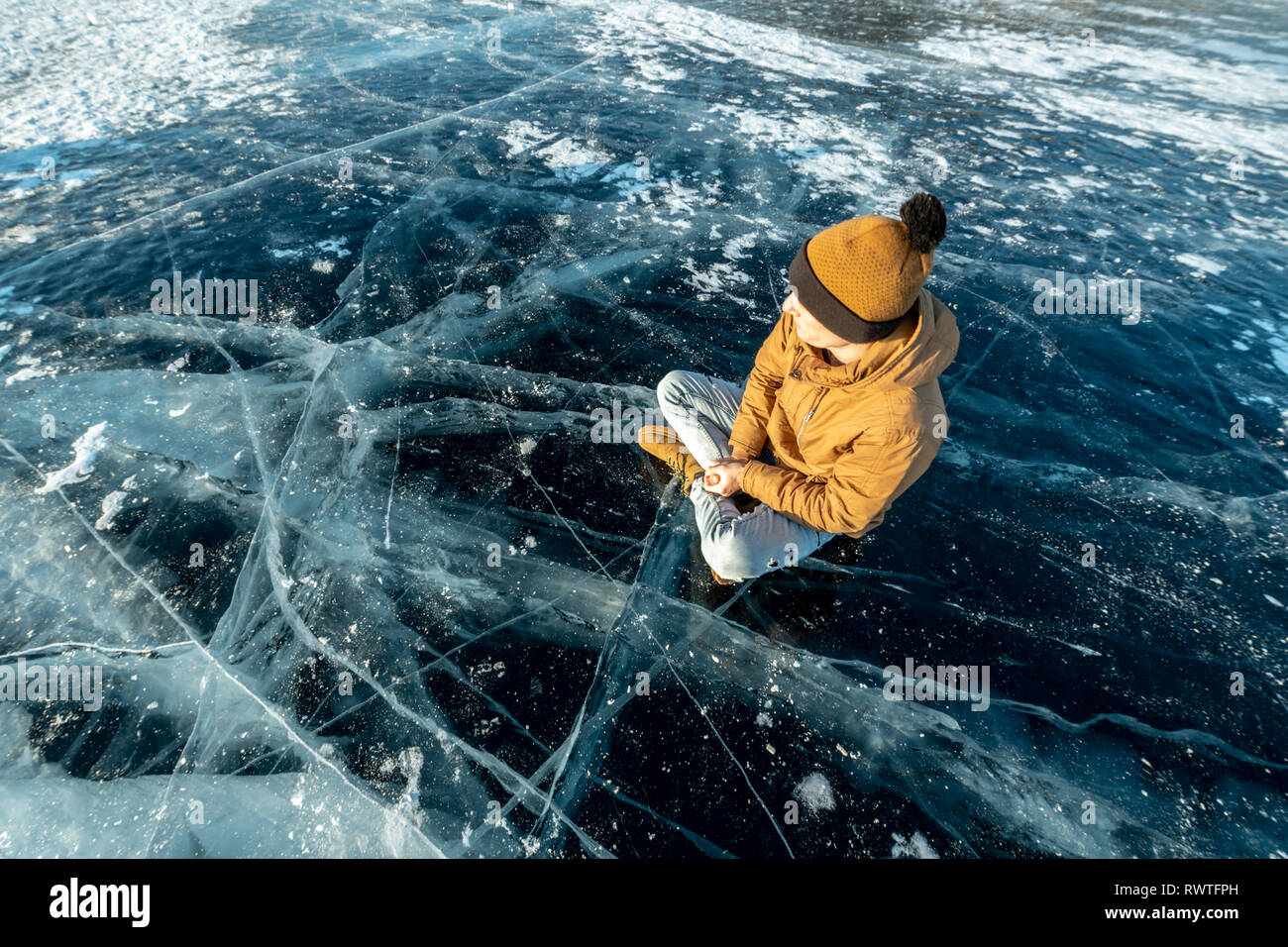 Tourist traveler medita seduti nella posizione del loto sul puro e trasparente di ghiaccio del lago Baikal. Viaggiare a bellissimi luoghi della natura Foto Stock