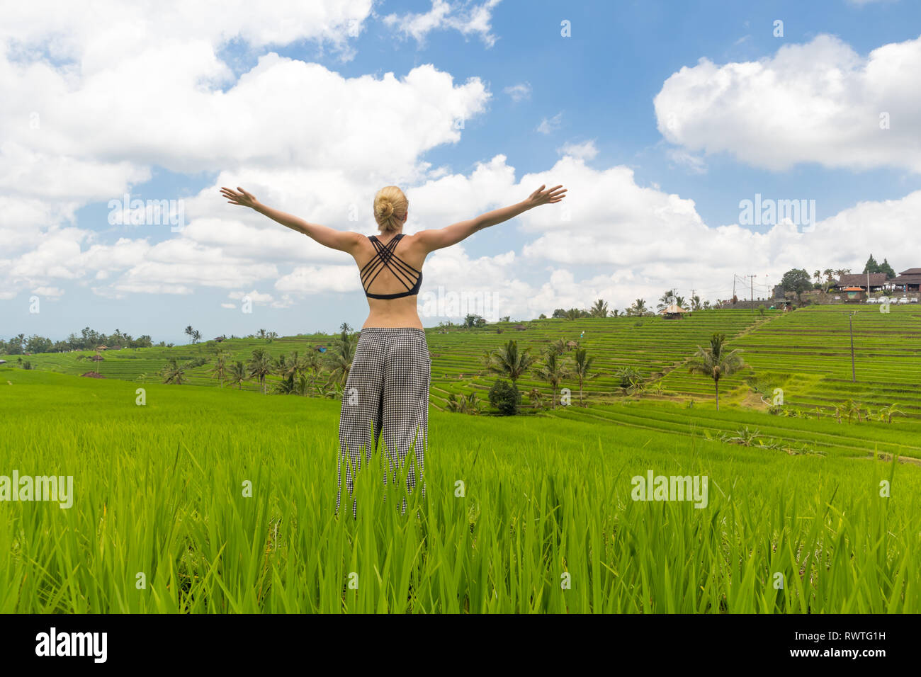 Rilassato e informale donna sportivo, bracci fatto alzare al cielo, godendo di pura natura di splendidi e verdi risaie di Bali. Foto Stock