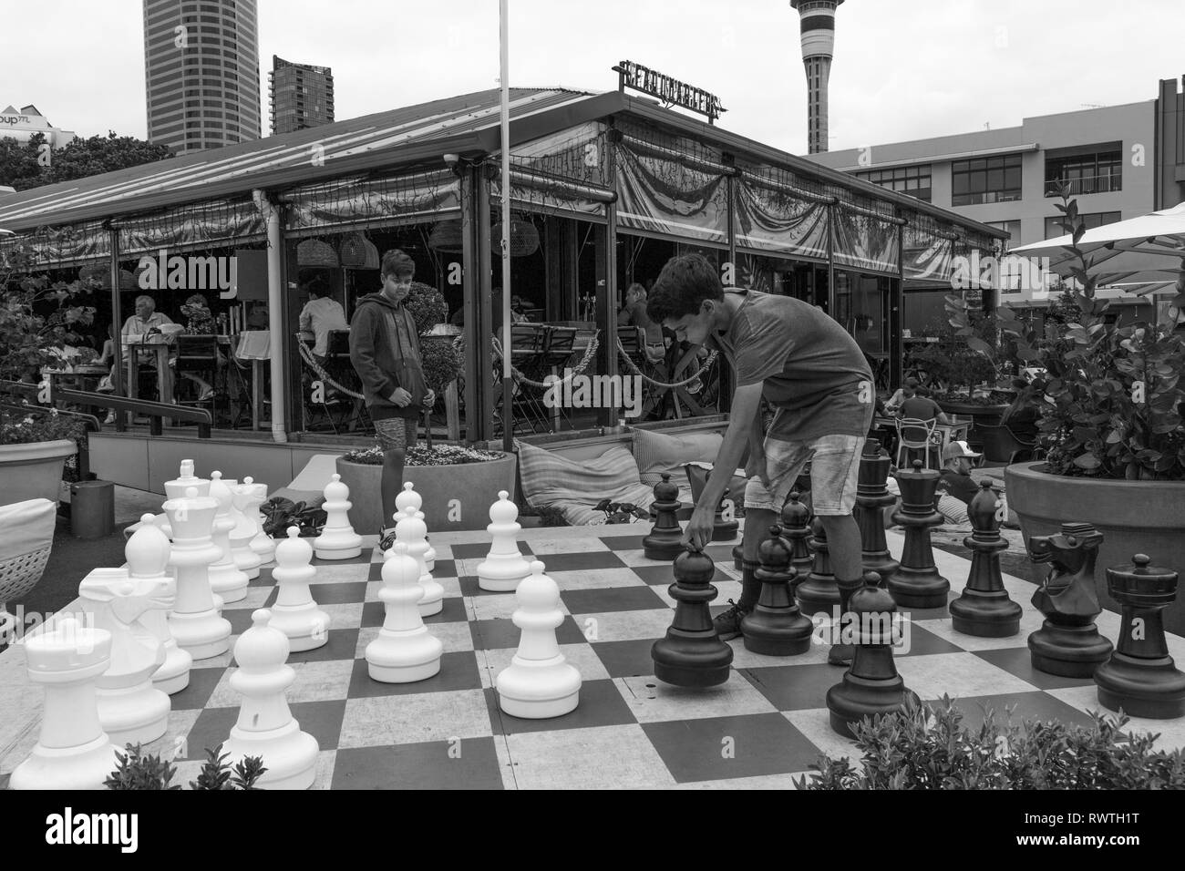 Mar Gen 1° 2019,Auckland Nuova Zelanda - due ragazzi adolescenti giocare una partita a scacchi su una grande scacchiera esterna con grandi pezzi di scacchi. Foto Stock