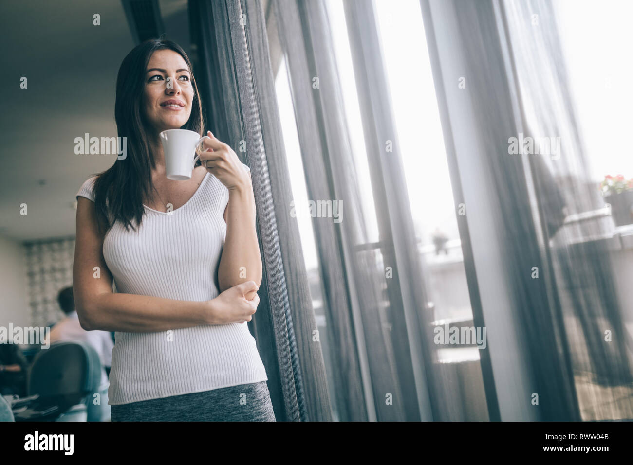 Imprenditrice con caffè o tè guardando lontano. Sorridente e azienda tazza da tè break dopo la riunione Foto Stock