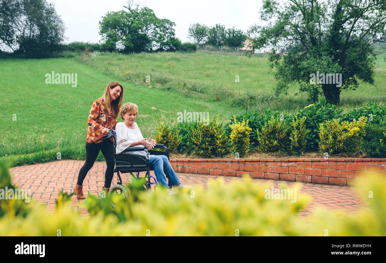 La donna che porta la sua madre in una sedia a rotelle Foto Stock