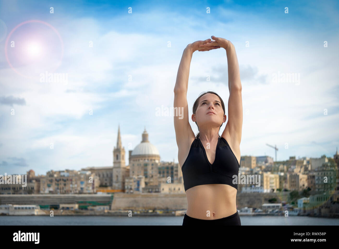 Vista frontale di una donna facendo un tratto del braccio esercizio di riscaldamento. La Valletta Malta sfondo. Foto Stock