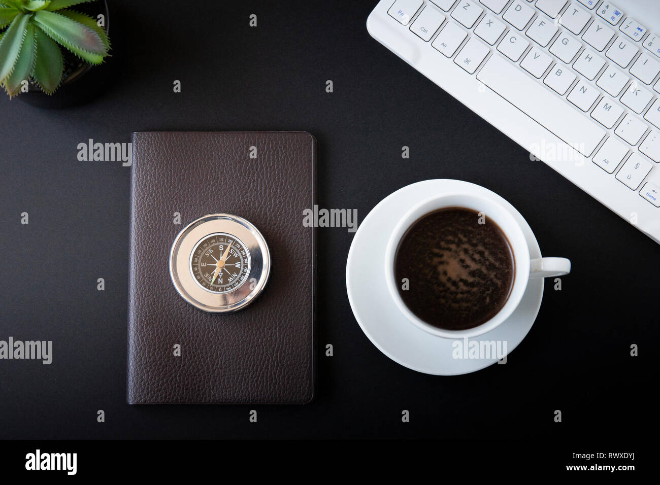 Office desk top view o laici piatta con sfondo nero, bianco tastiera, tazza di caffè, bussola metallica e una piccola succulenta. Foto Stock