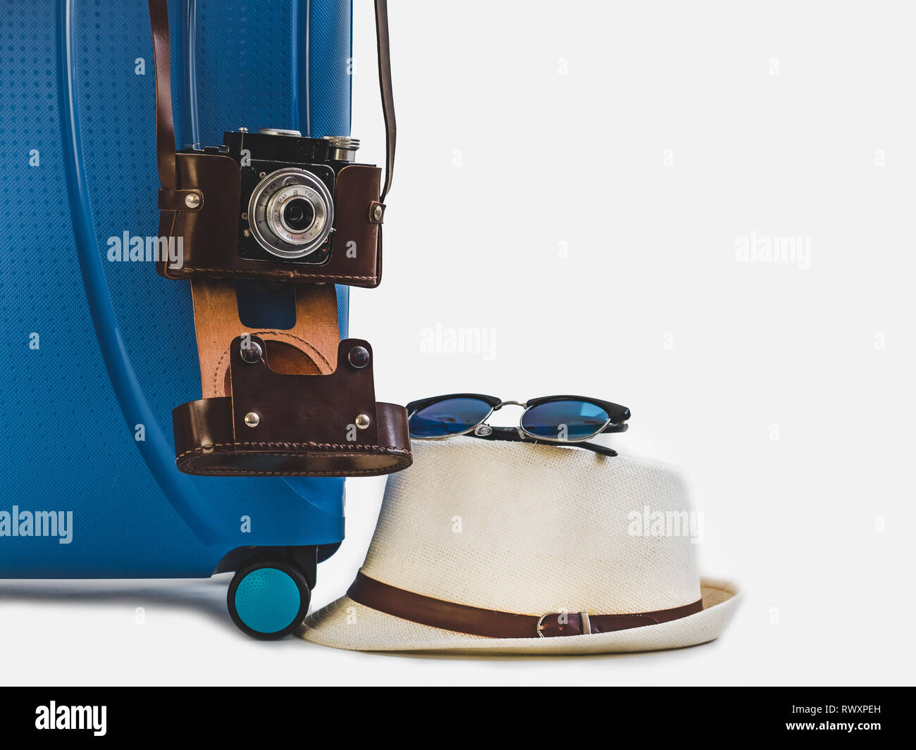 Elegante, blu valigia, Elegante cappello per il sole, vintage fotocamera in un marrone custodia in pelle. Bianco, isolato sfondo. Close-up. Vista laterale. Preparazione per TH Foto Stock