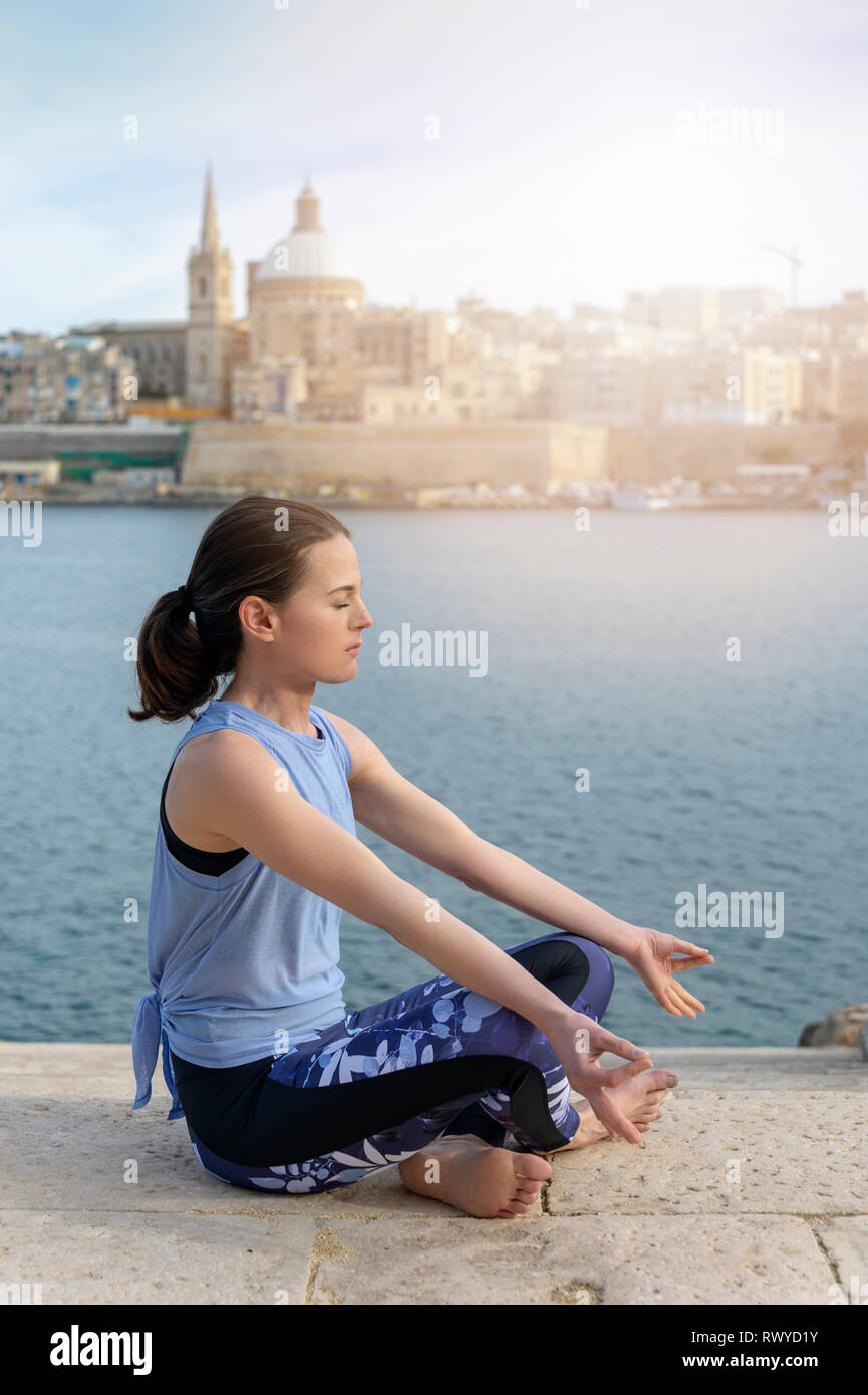 Vista laterale di una donna meditando, la pratica dello yoga con La Valletta, Malta come sfondo Foto Stock